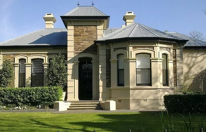 Beautiful tan and brown stone house on a property with a green yard and black fence.