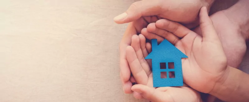 Adult and child hands holding blue paper house for asset protection and inheritance concept.