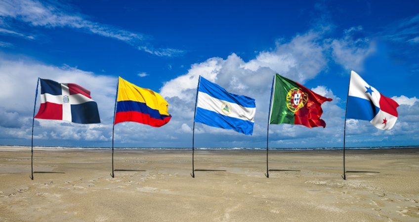 the flags of panama, colombia, nicaragua, portugal and dominican republic flapping in the wind on a beach