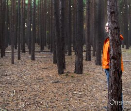 Man in Bright Orange Jacket Hiding Behind A Tree