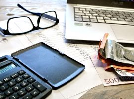 A desk with laptop, glasses, calculator, and euros