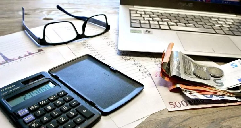 A desk with laptop, glasses, calculator, and euros