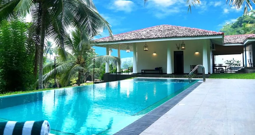 a view of a pool with a house, blue sky and plants