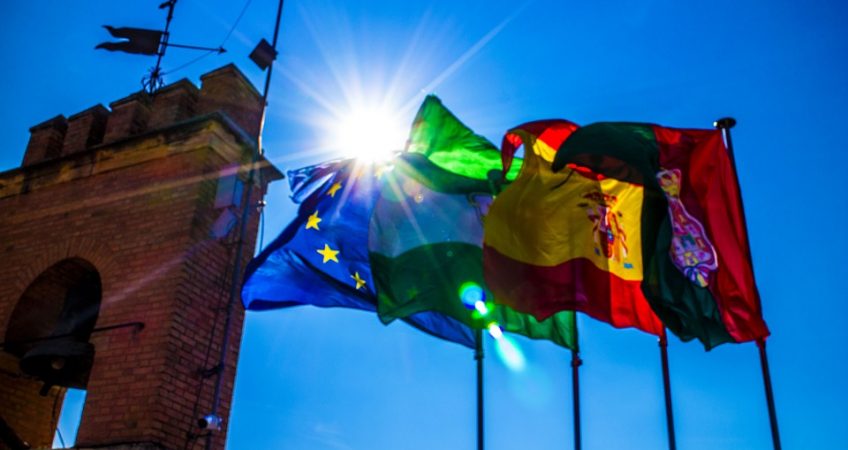 EU, Portugal and Spanish Flag flying with blue sky and sun in the background