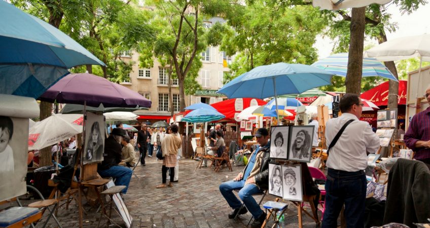 street scene in montemarte paris. artists painting customers who are sheltering under umbrellas underneath spring trees