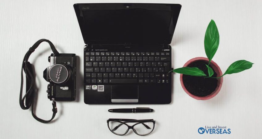 Desk with a laptop, plant camera pen and pair of glasses