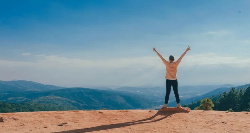 Person stands on top of a mountain celebrating