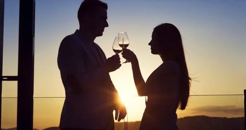 silhouette of 2 people drinking wine in contrast with the sun