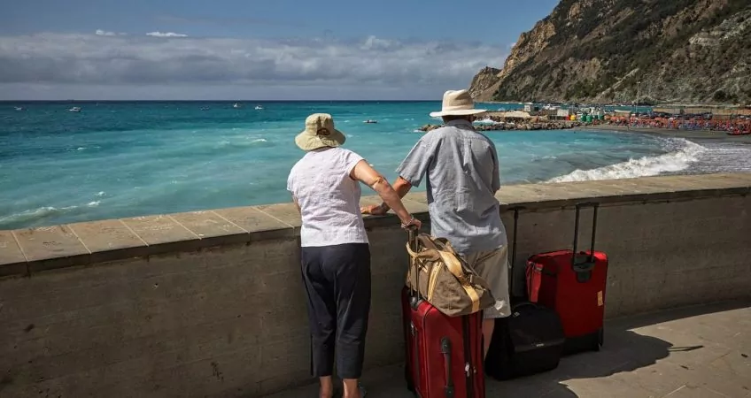 Older travellers with suit cases looking out to sea