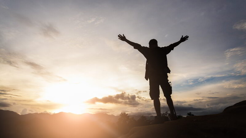 Silhouette of man standing on top of hill and enjoying sunrise over the valley.