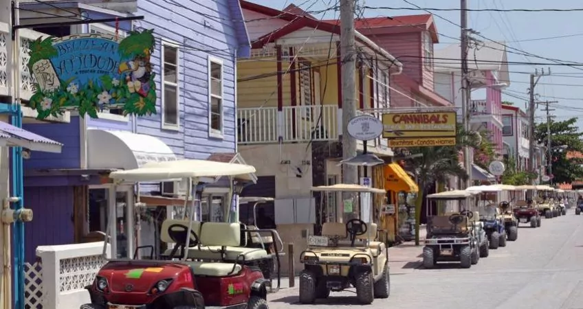 Golf carts parked in line on th eside of the rode with colorful houses on the side in a street on ambergris caye, belize