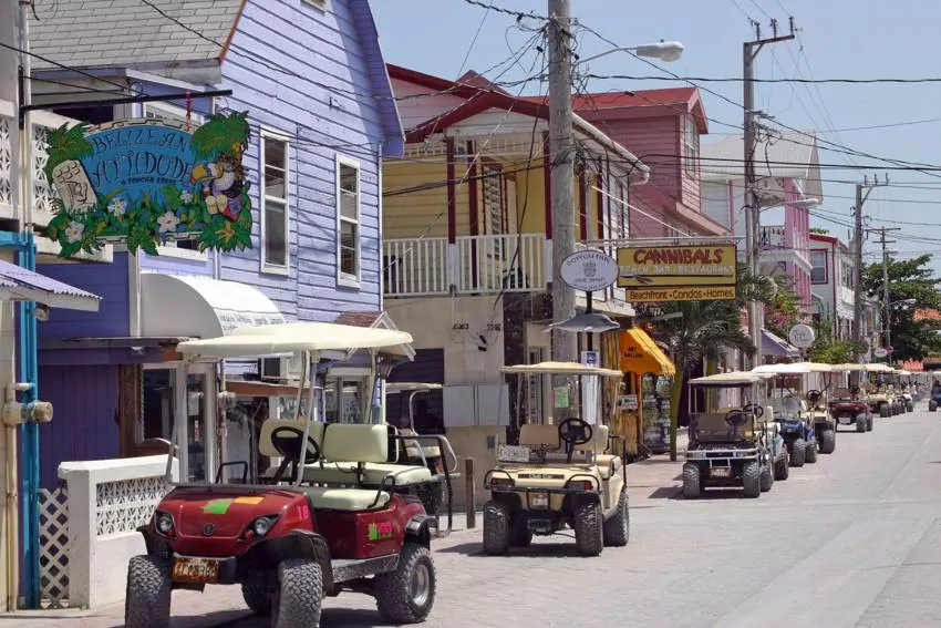 Golf carts parked in line on th eside of the rode with colorful houses on the side in a street on ambergris caye, belize