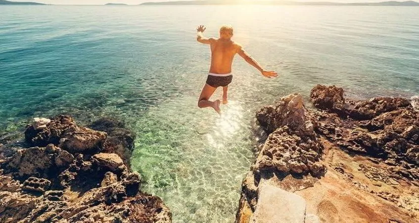 a man jumping from a cliff into the ocean