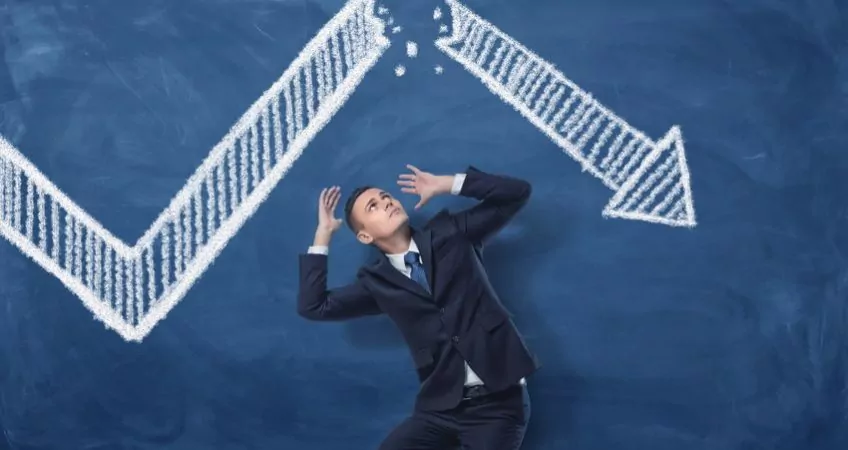 A businessman underneath a falling arrow on finance chart