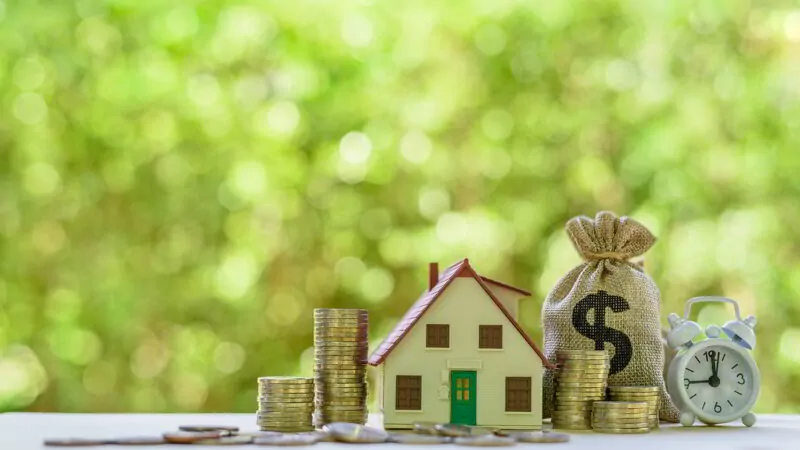 Diversifying investments concept. House model, coins, US dollar bag, white clock on a table.