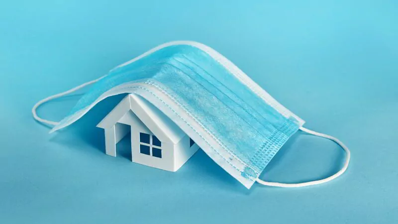 Paper house model cover by a mask isolated on blue background.