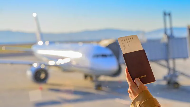 Passport and boarding pass in hand of passenger waiting at the gate.