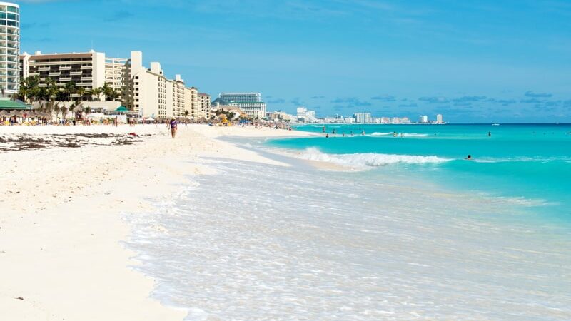 Tourists enjoy the sunny weather and relaxing on the beautiful beach in Cancun, Mexico.