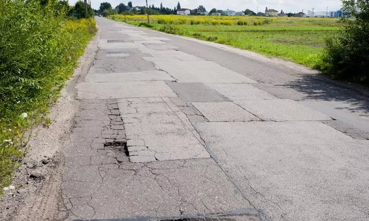 Many chuckholes in asphalt damaged road.