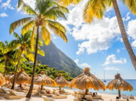 Caribbean beach with palms and straw umbrellas on the shore with Gros Piton mountain in the background, Sugar beach, Saint Lucia