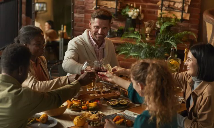 Multi-ethnic group of people clinking glasses while enjoying dinner party with friends and family in cozy interior