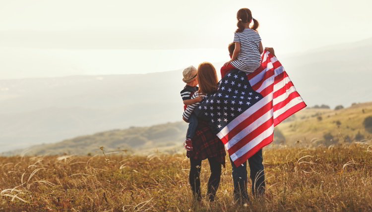 Happy family with American flag at sunset outdoors