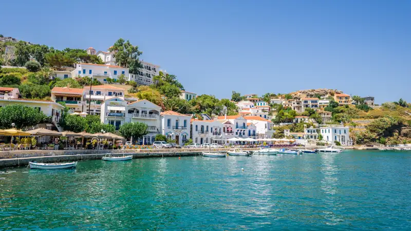 Beautiful sunny greek village town white house and harbor view to the aegean blue sea with crystal clear water and fishing boats cruising yacht white houses, Ikaria Island, Evdilos, Sporade, Greece