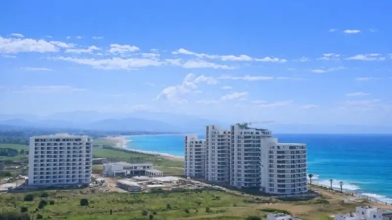 Modern beachfront apartment developments along a long sandy coastline in Northern Cyprus with clear blue Mediterranean waters.