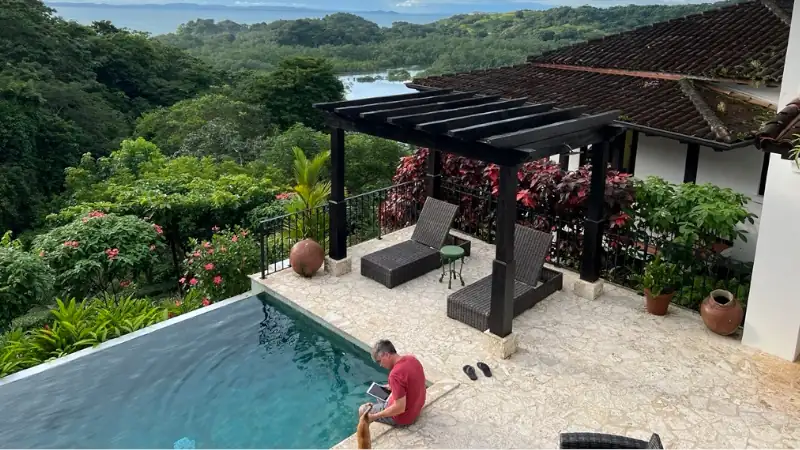 Lief reading by a pool at a hillside home with lush tropical views.