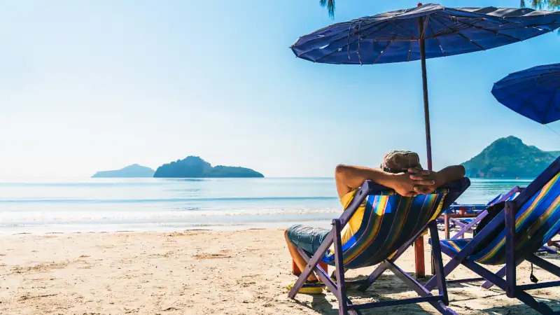 Summer lifestyle Asian man traveler relaxing on beach chair in front of vacation exotic beach, Attraction place leisure tourist travel Hua Hin Thailand holiday trip, Tourism beautiful destination Asia