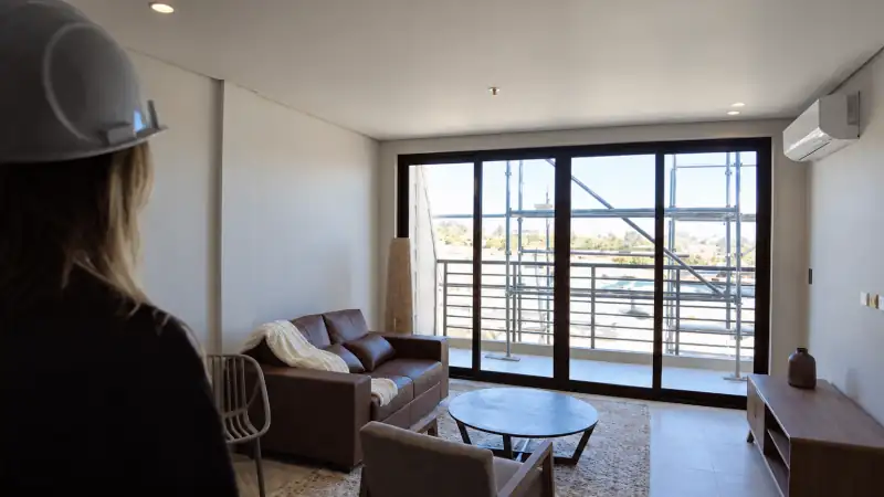 Sophia looks into a bright, modern apartment living room with a balcony beyond the sliding glass doors.